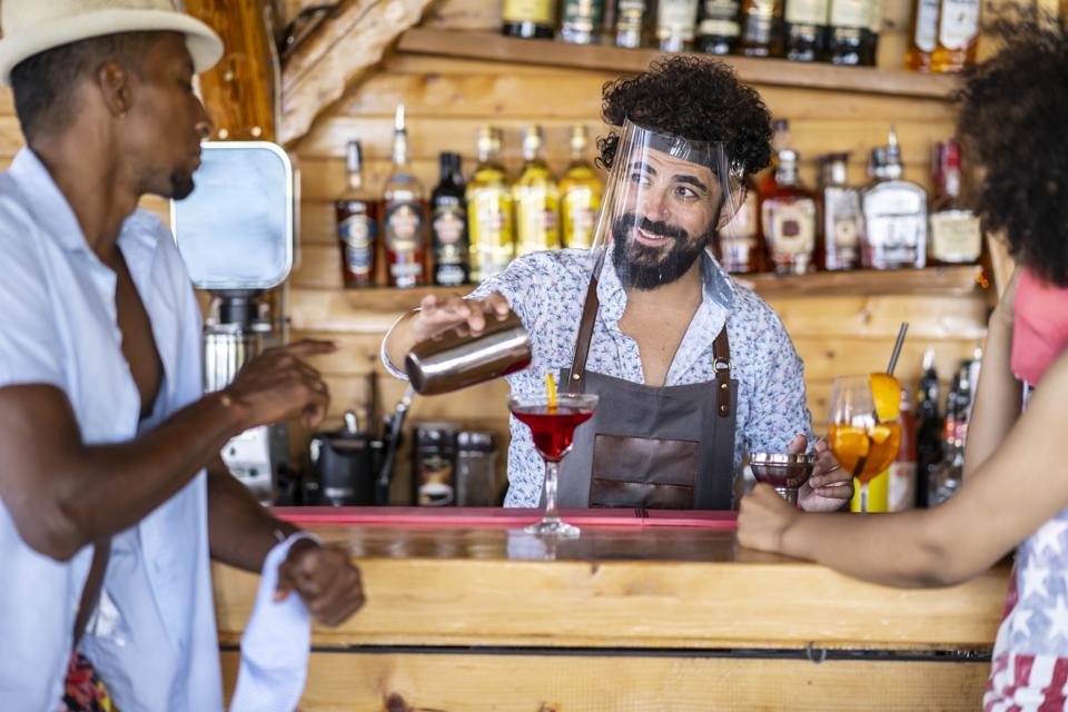 Bartender wearing face shield for protection of illnesses and viruses.