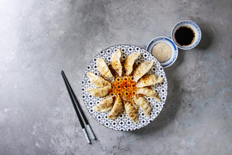 Asian dumplings Gyozas potstickers on white blue ceramic plate served with chopsticks and bowl of soy sesame sauce over grey texture background Top view, copy space