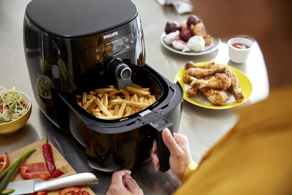 Philips air fryer filled with French fries, sitting next to chicken drumsticks