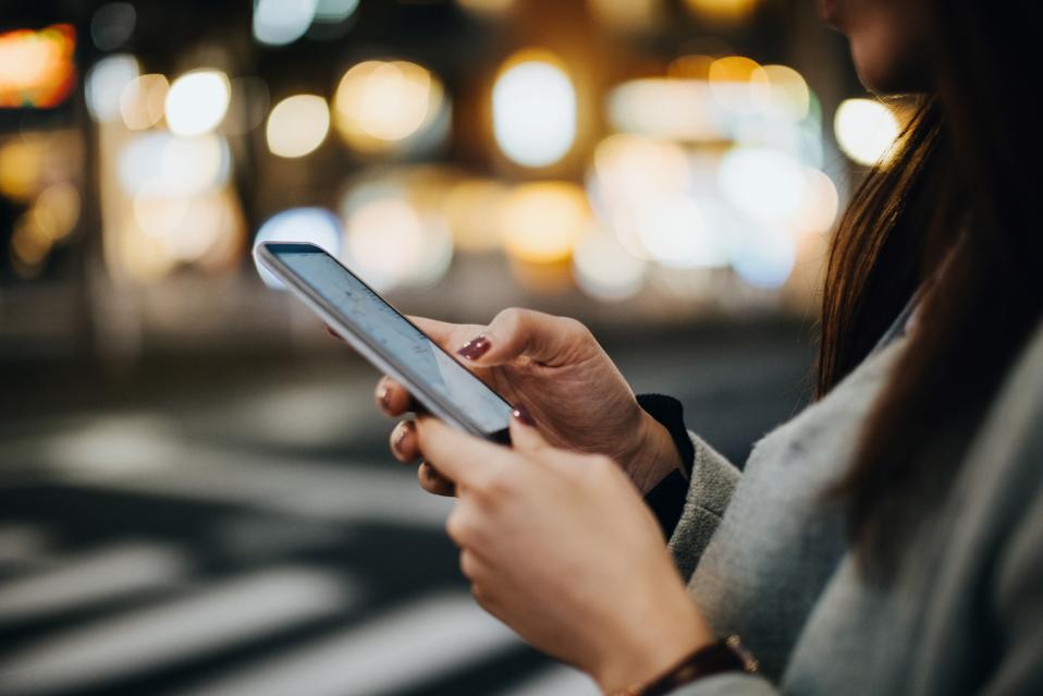 Close up of woman navigating location with smartphone in busy city street at night