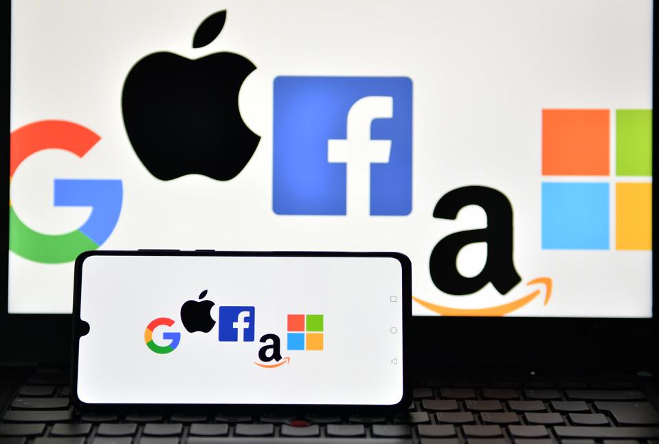 Logos of Google, Apple, Facebook, Amazon and Microsoft displayed on a mobile phone and a laptop screen.