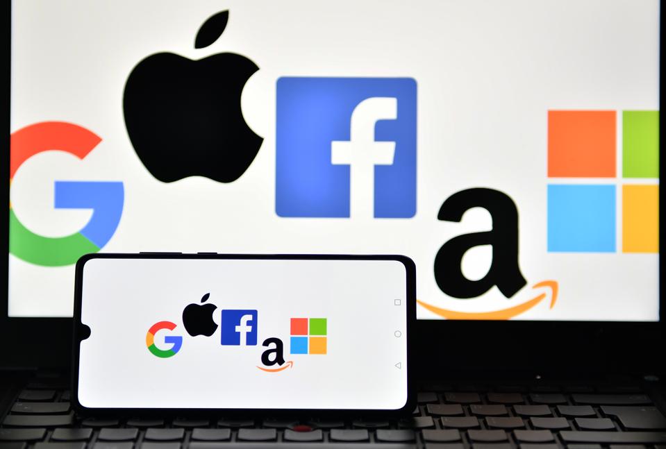 Logos of Google, Apple, Facebook, Amazon and Microsoft displayed on a mobile phone and a laptop screen. 