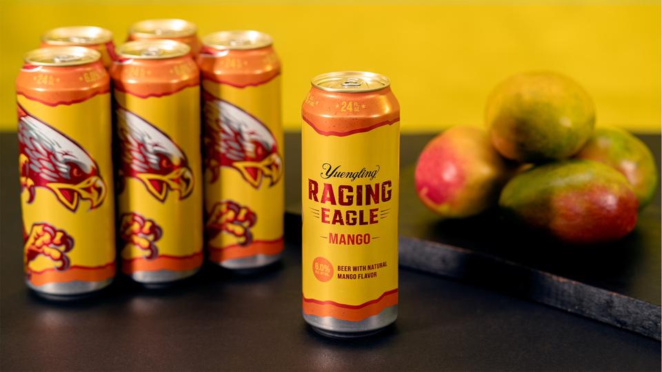 Red and yellow cans of beer next to mangos
