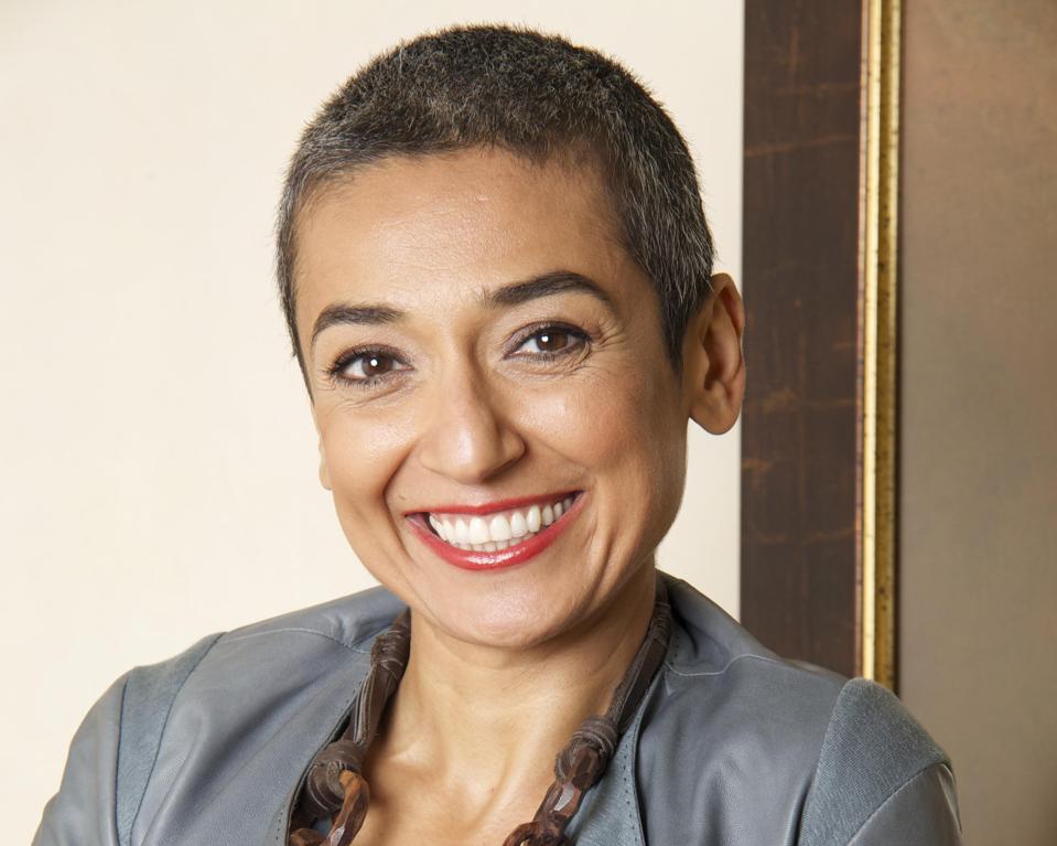 Portrait of a smiling woman, with a necklace and grey outfit.