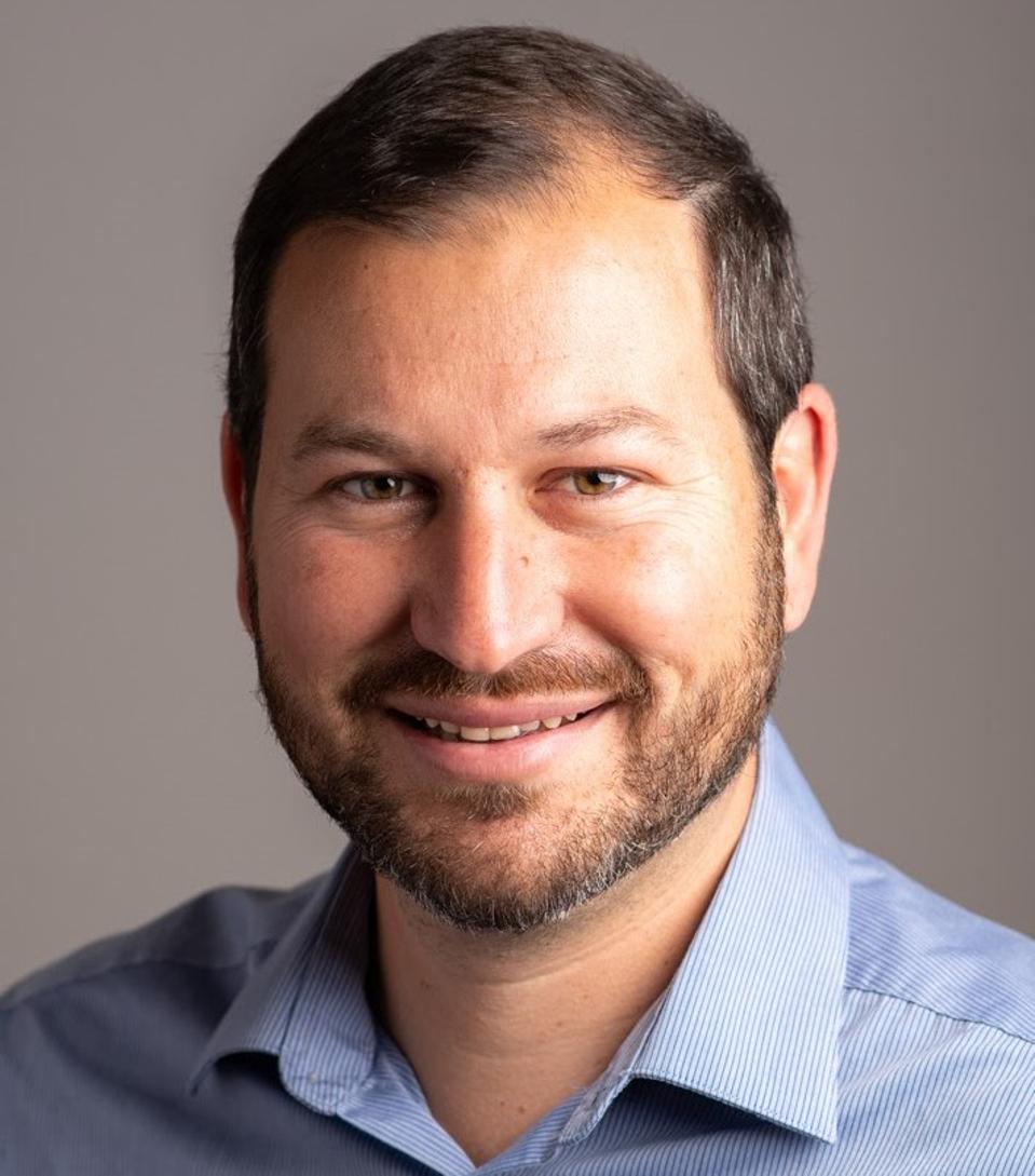 A man wearing a blue collared shirt smiling into camera