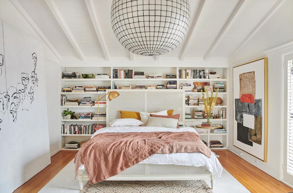 An airy bedroom with a bookshelf and art.