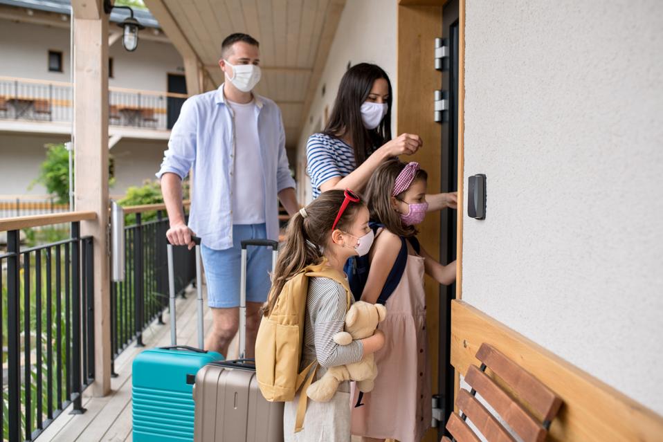 Family with children and face masks outdoors by hotel in summer, holiday concept.