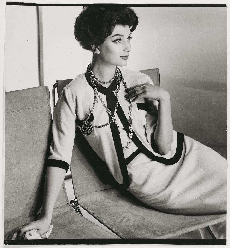 Henry Clarke. Marie-Hélène Arnaud in a Chanel three-piece suit in white wool jersey edged with navy blue jersey sporting a Chanel necklace. Published in Vogue US on March 1, 1958