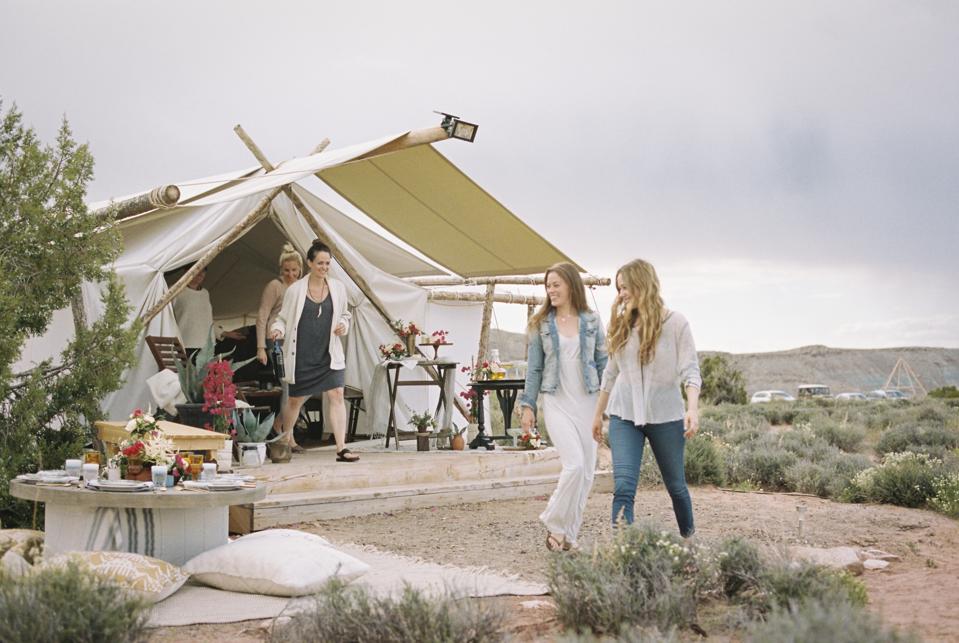 Group of friends glamping enjoying an outdoor meal, a tent in the background.