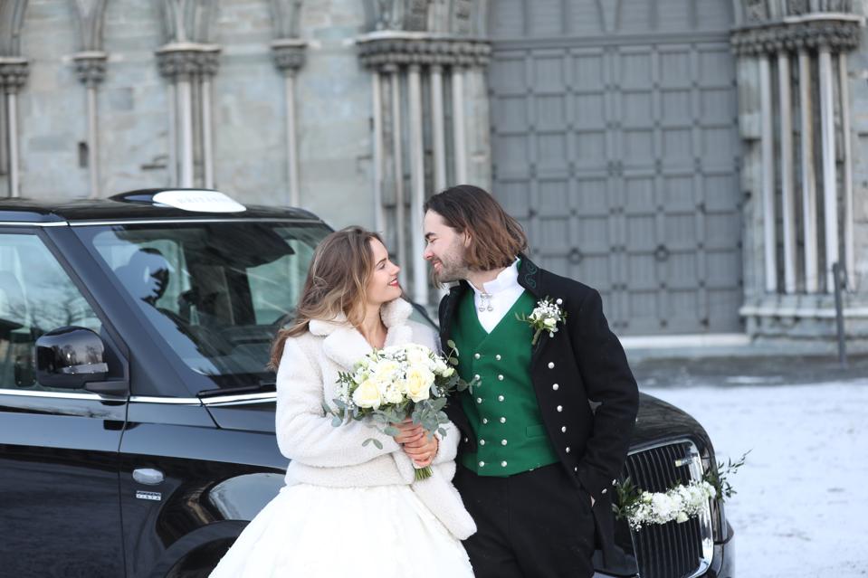 A bride and groom stand in front of a vintage London Black Cab in Trondheim, Norway
