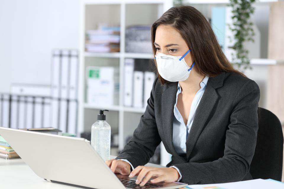 Exécutif portant un masque travaillant sur un ordinateur portable au bureau