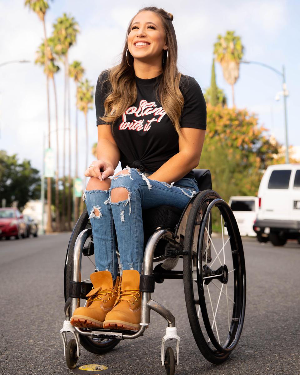 Chelsie Hill smiles in a wheelchair on a sunny street.