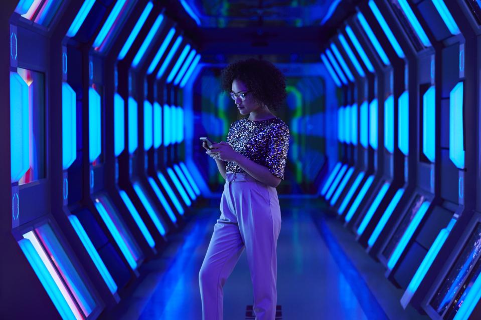 Young businesswoman looking at smartphone in spaceship like corridor