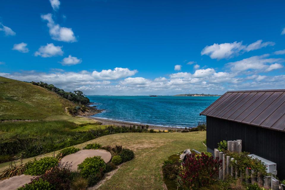 View of the blue waters at the edge of a green island with a black house in the foreground