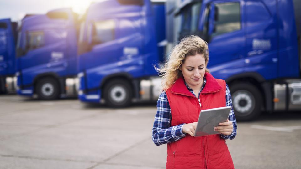 Truck driver holding tablet and checking route for new destination. In background parked truck vehicles. Transportation service.