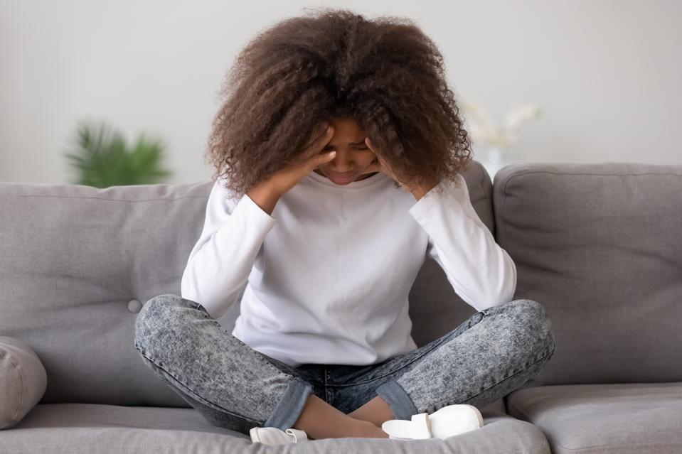 A young Black woman holding her head, as if in pain.