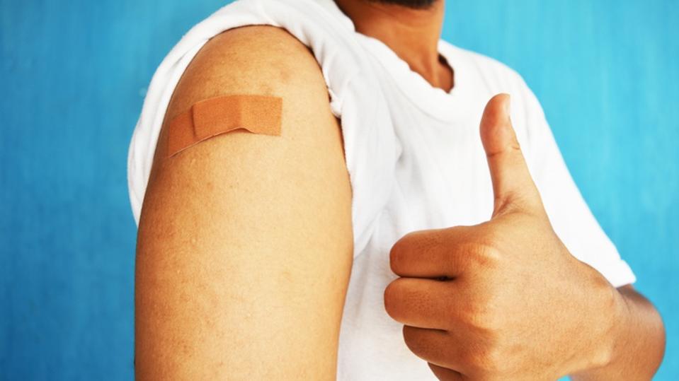 Asian man using adhesive bandage plaster on her arm showing thumb up gesture after injection vaccine.