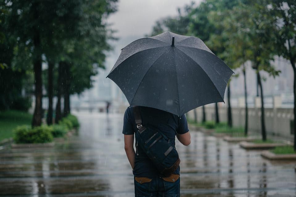 Rear view of male holding umbrella in rainy city