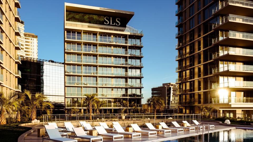 A tall hotel building next to a pool lined with chairs