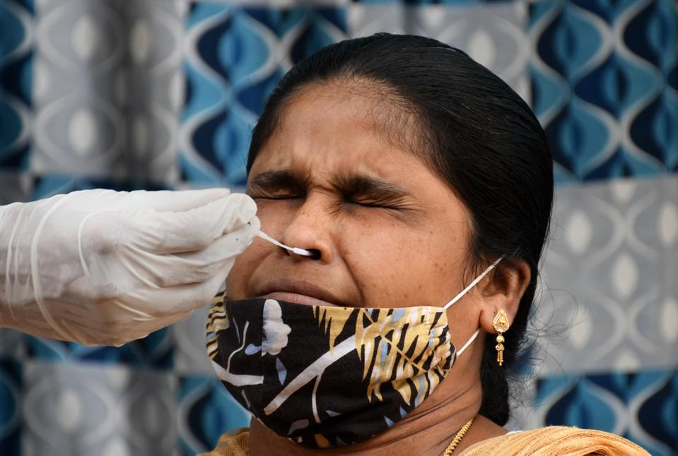A healthcare worker collects a swab sample from a woman...