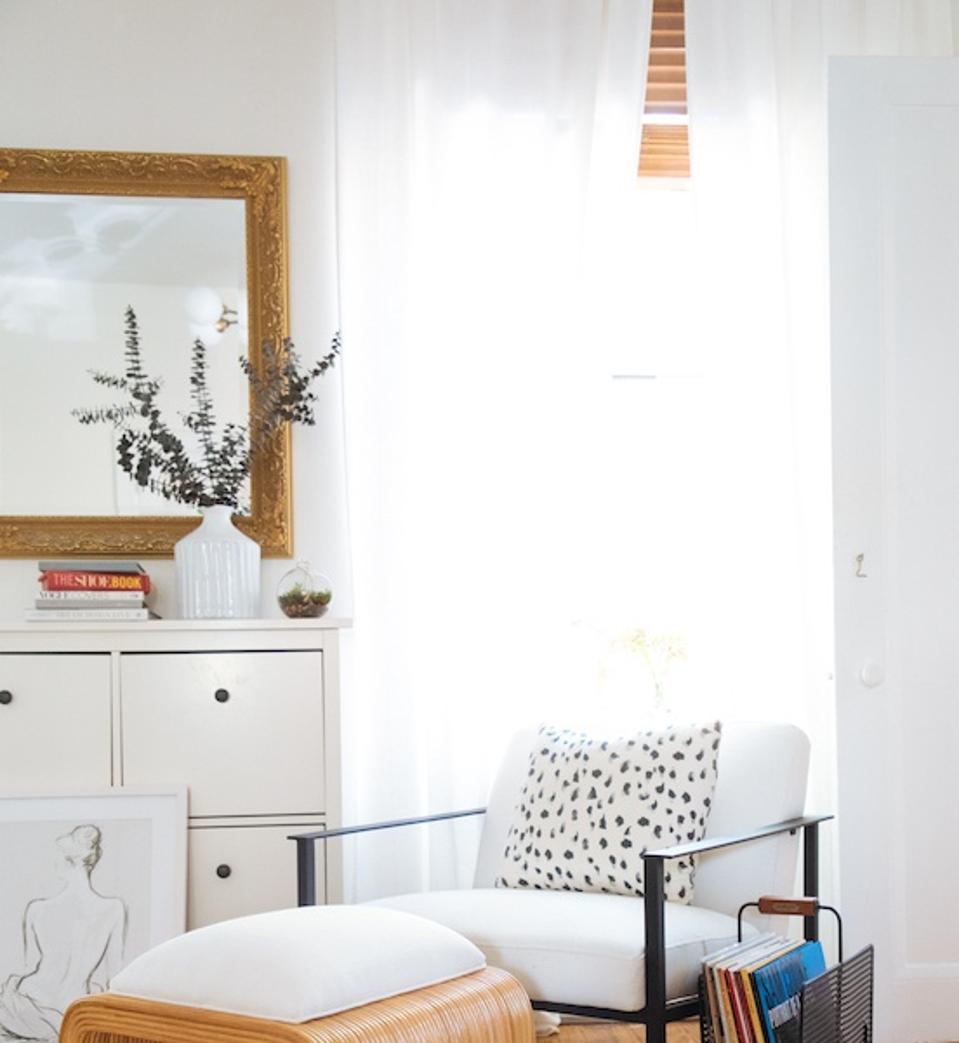 A corner with a white curtain, chair and Dalmatian style pillow