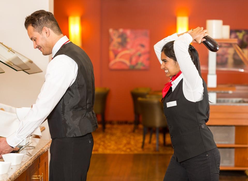 Frustrated waitress trying to hit colleague with cucumber