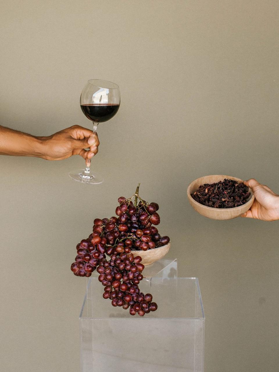 A wine glass, red grapes, and herbs.