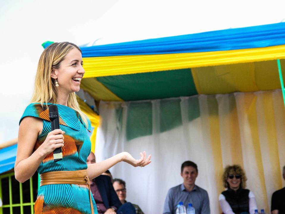 Wallace, in a blue dress, speaks to several people under a blue and yellow awning