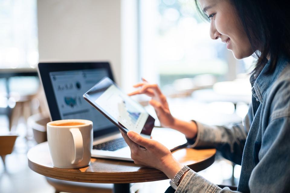 Businesswoman looking at financial data on tablet and laptop with a coffee