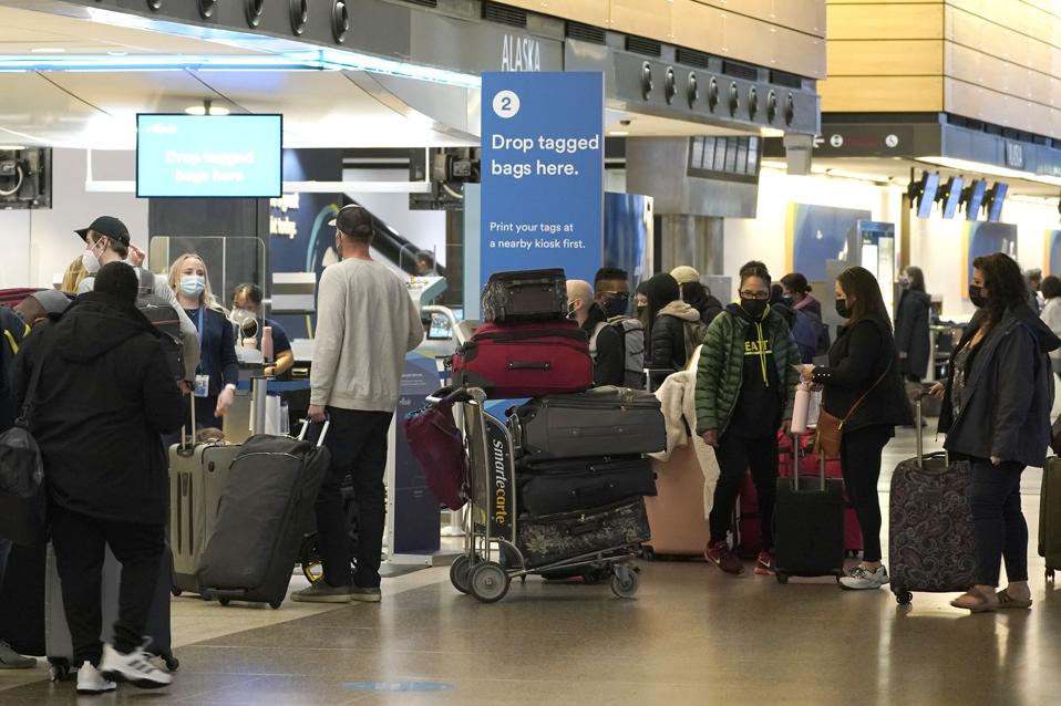 Passengers wearing masks wait in line with luggage near an Alaska Airlines check-in area at Seattle-Tacoma International Airport. A new survey says travelers are more likely to travel if destinations have vaccine requirements. (AP Photo/Ted S. Warren)