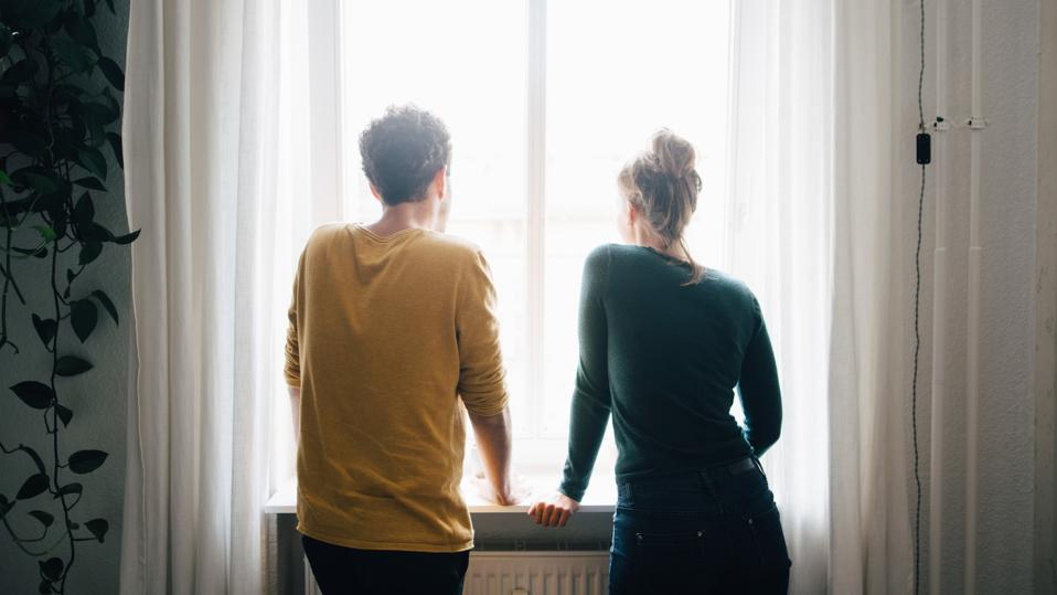 Rear view of couple looking through window while standing at home