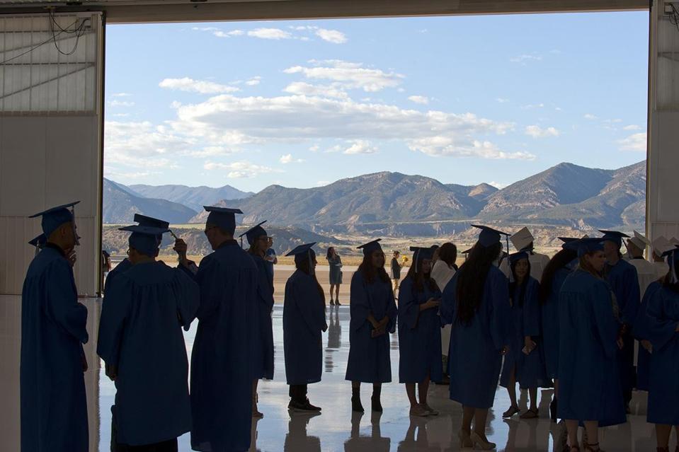 College graduates in shadow of mountain range.