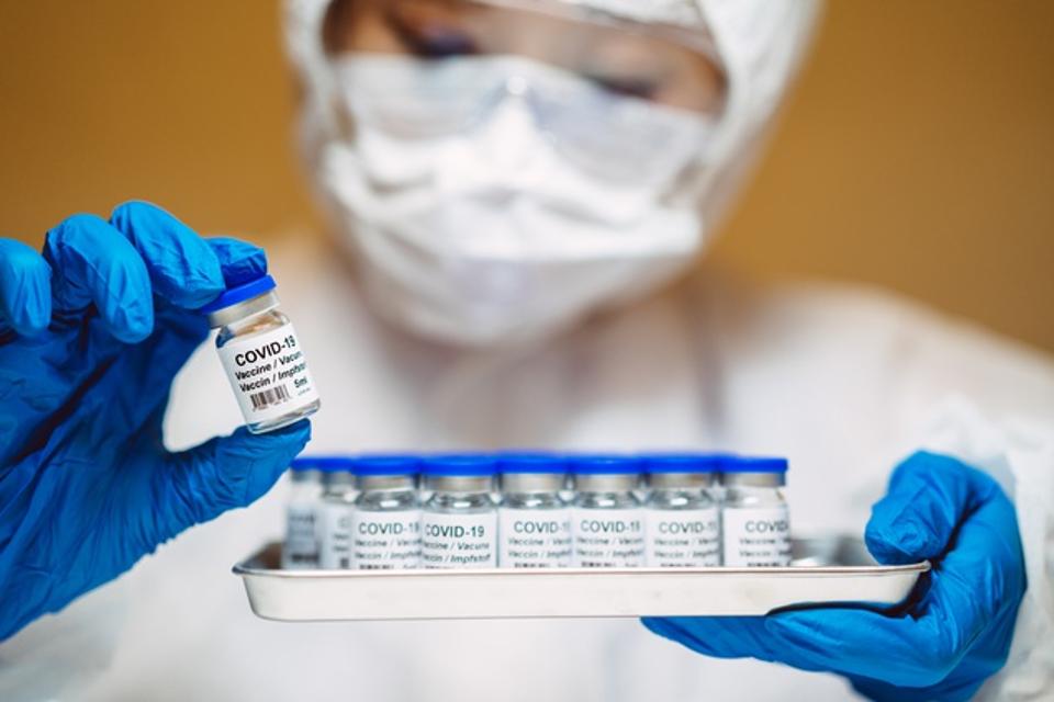 Healthcare professional in protective gloves & workwear holding & organising a tray of COVID-19 vaccine vials