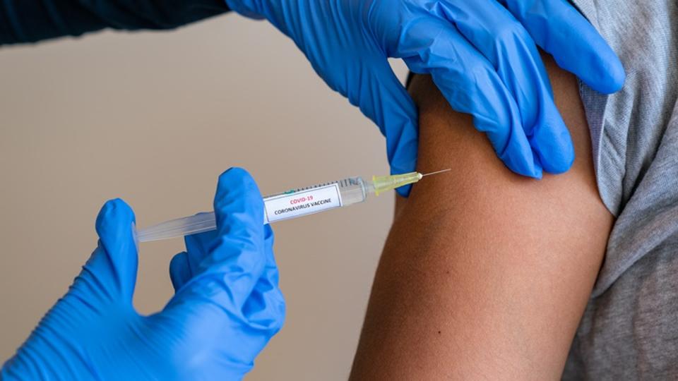 Female doctor wearing blue latex gloves injecting a child in her arm with a needle and syringe containing a dose of the COVID-19 vaccine cure by way of immunisation - 052