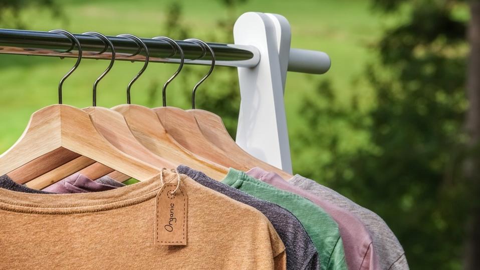 Organic clothes, t-shirts hanging on wooden hangers with green forest, nature in background.