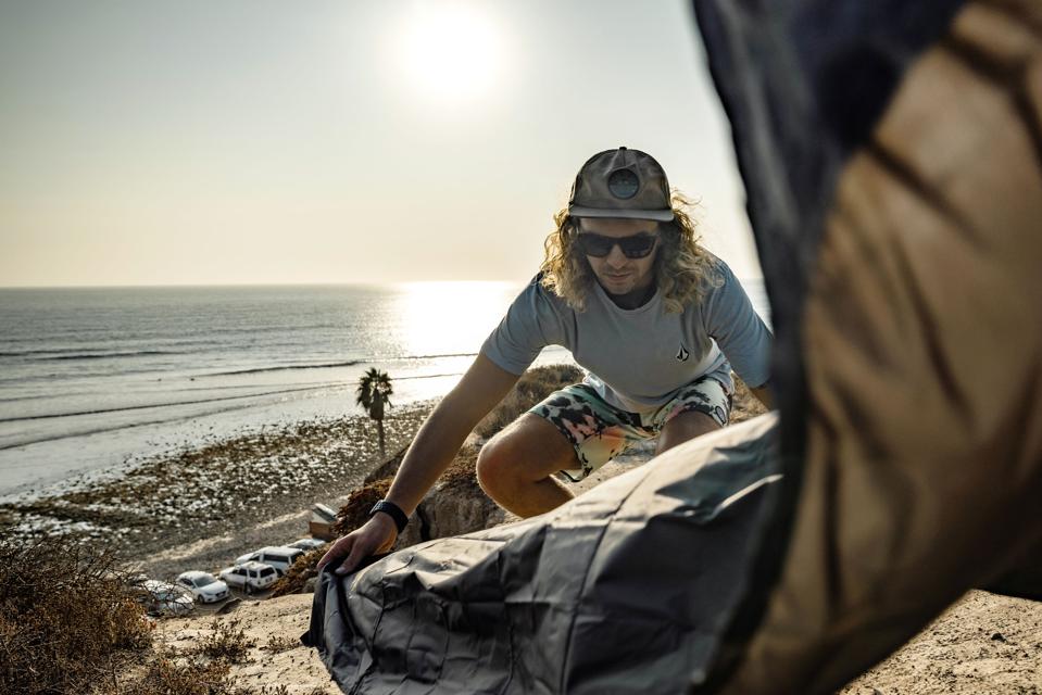 man opening travel blanket on cliff above beach