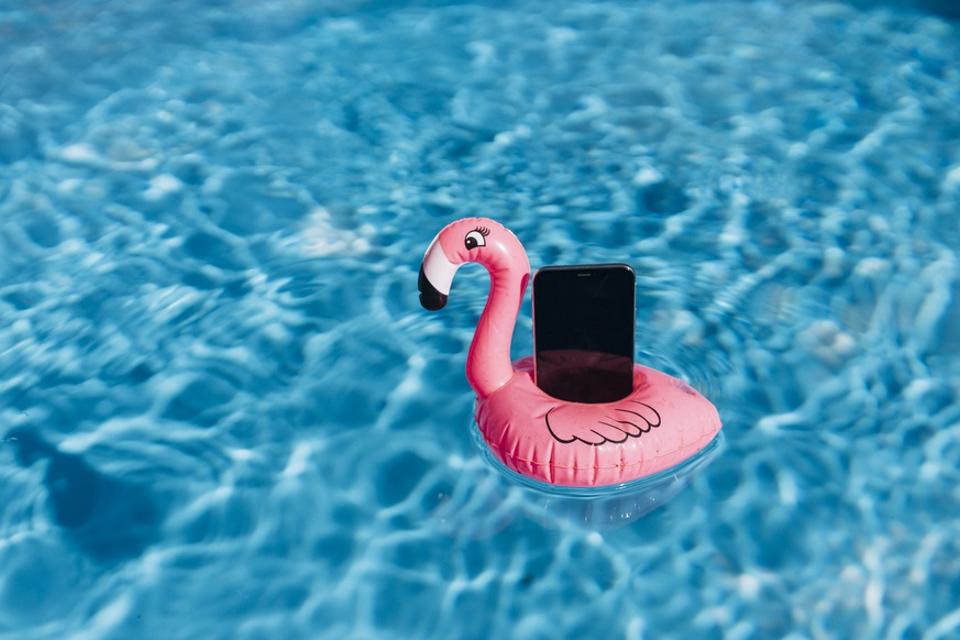 Smartphone on pink flamingo float in swimming pool