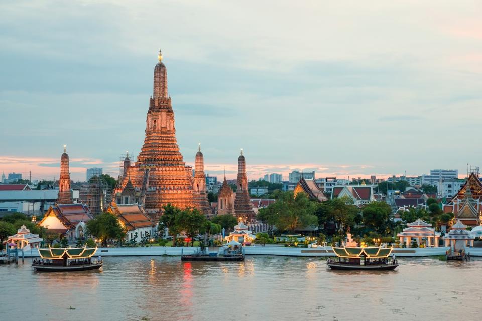 Wat Arun towers above other buildings next to the river with a few Thai boats in the foreground