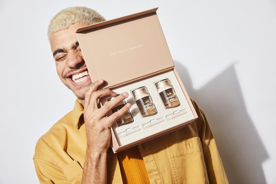 Guy holding a box of three amber colour transparent bottles of perfume