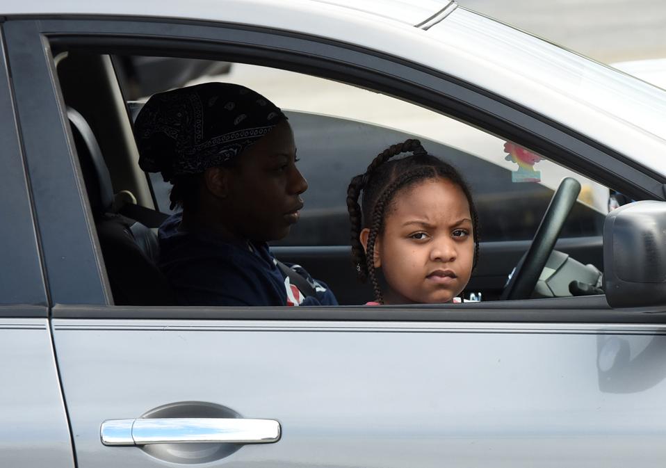 A child and her mother wait in their car at a food...