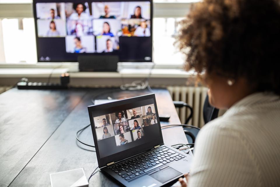 Woman watching teleconference meeting on laptop and monitor.