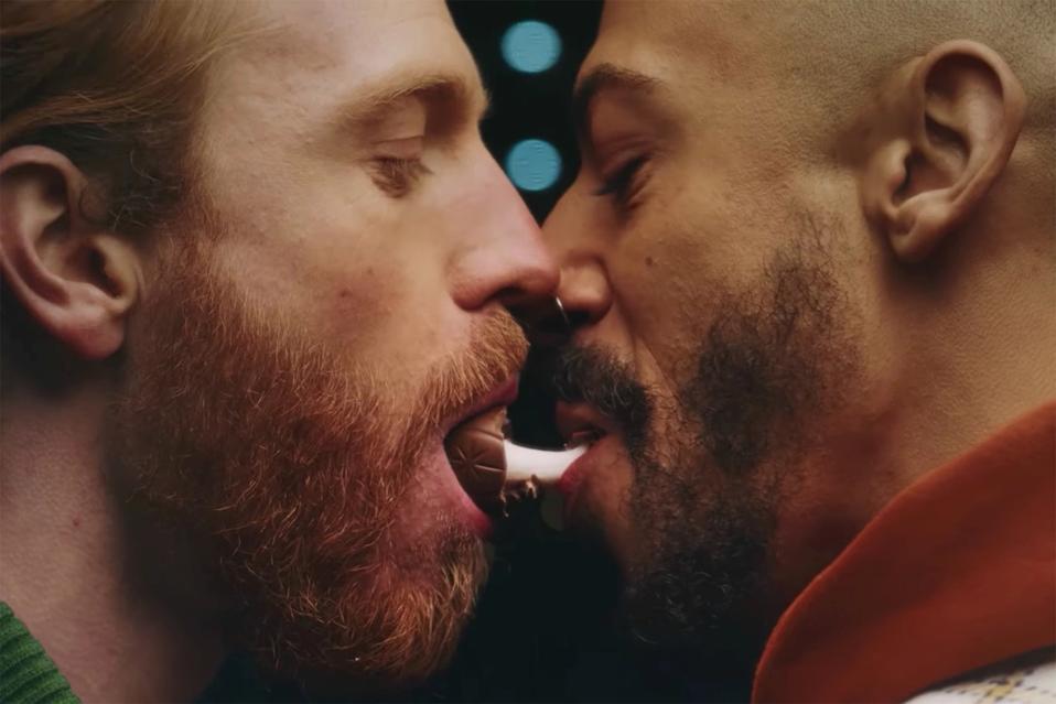 Two gay men kiss as they enjoy a Cadbury candy.