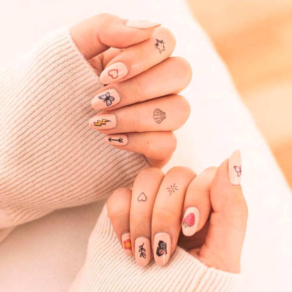 two female hands with nail art on each nail and tattoo on four fingers