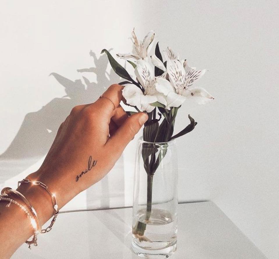 hand with tattoo touching a flower in vase
