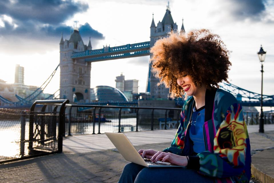 Young girl sitting outdoors, using laptop, Tower Bridge in background, London, England, UK