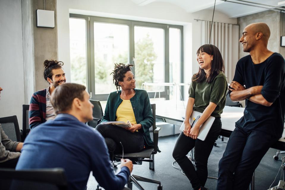 Colleagues looking at cheerful businesswoman in meeting