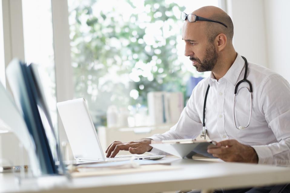 Concentrated doctor working with laptop at desk in office