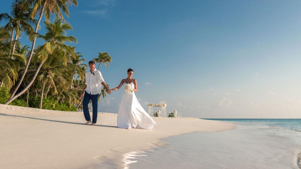 A newly married couple holding hands on Velaa Private Island.