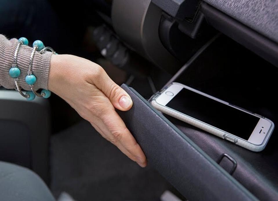 A drivers is putting her cell phone in a glove department.