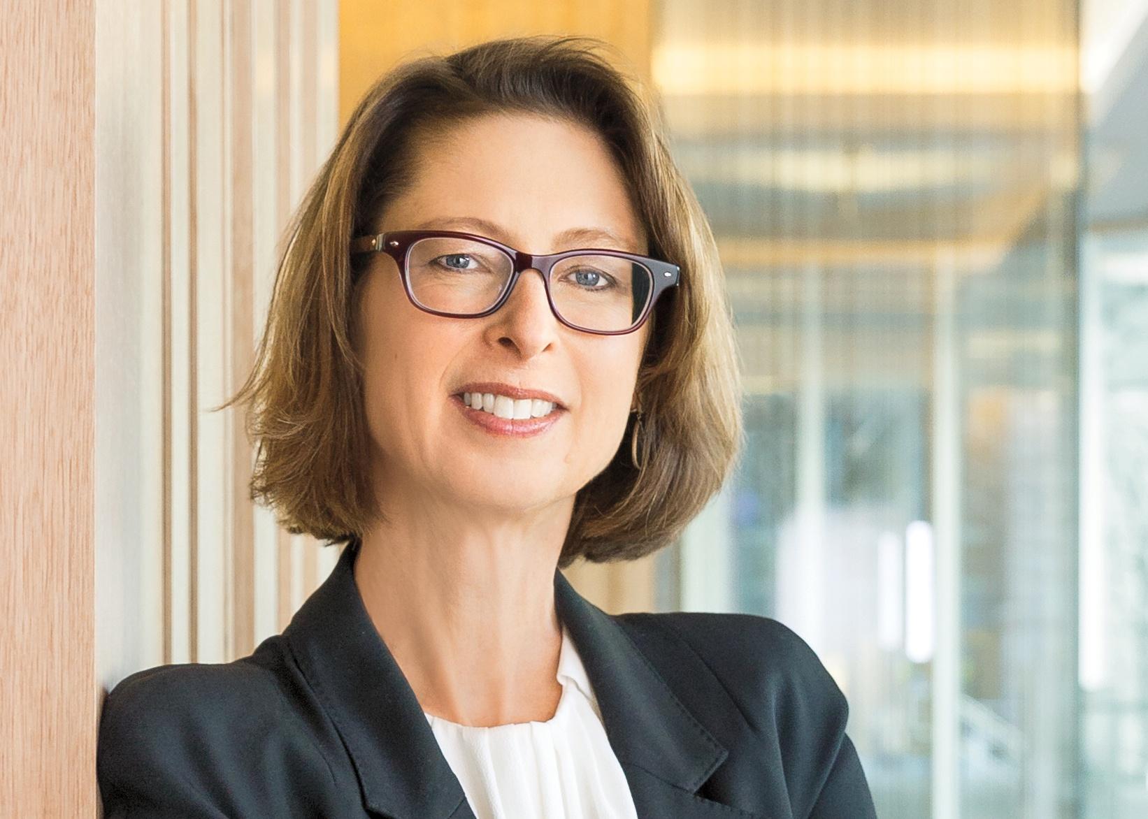 White woman with chin length brown hair wearing glasses and a blazer.